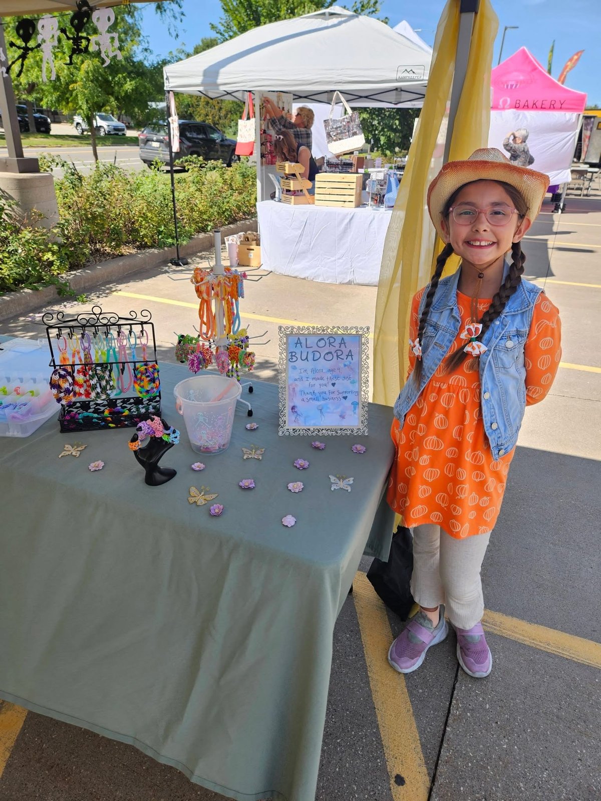 Alora standing proudly beside her Alora Budora jewelry market display